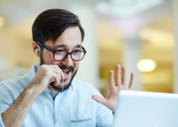 man talking into microphone and waving at computer