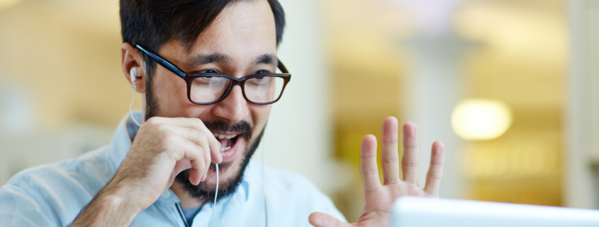 man talking into microphone and waving at computer