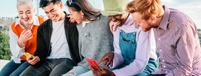Five multiracial friends watching videos on smartphones