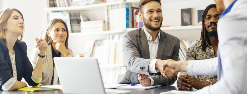 two men shaking hands at a table with others