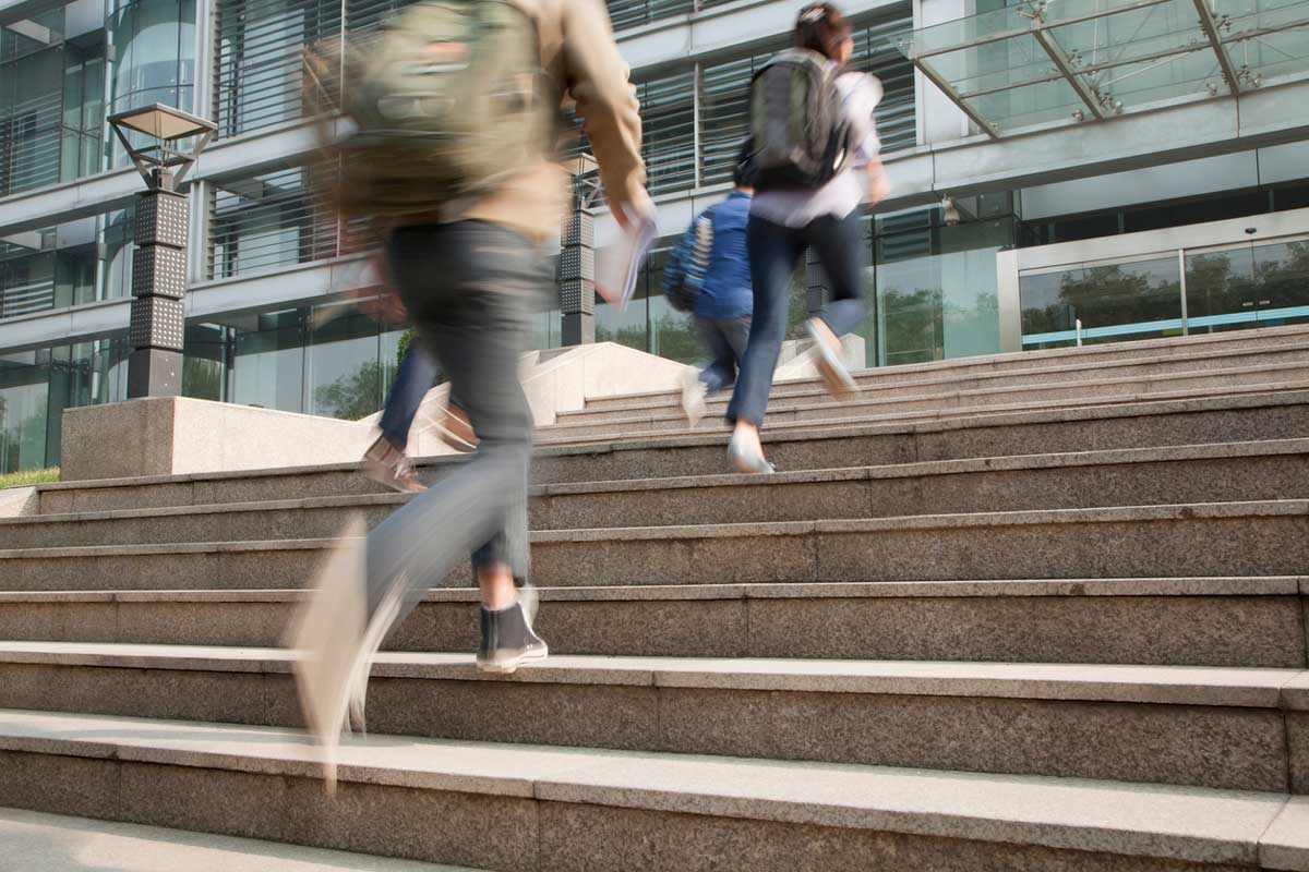 Late students with backpacks running up the stairs to school