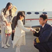 Customer-service Smiling pilot kneeling and talking to a young girl near an airplane