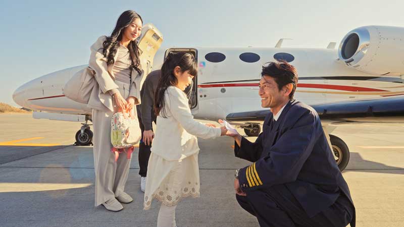 Smiling pilot kneeling and talking to a young girl near an airplane