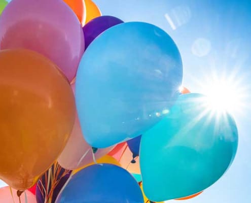 A bunch of balloons with the sun peeking out behind them