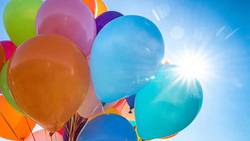A bunch of balloons with the sun peeking out behind them