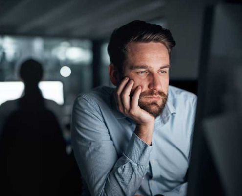 Bored man sitting at a computer in a dark office