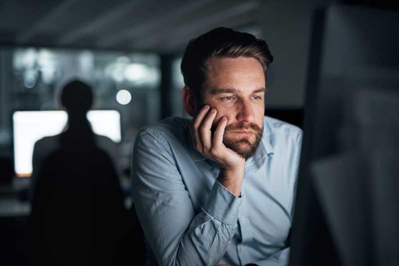 Bored man sitting at a computer in a dark office