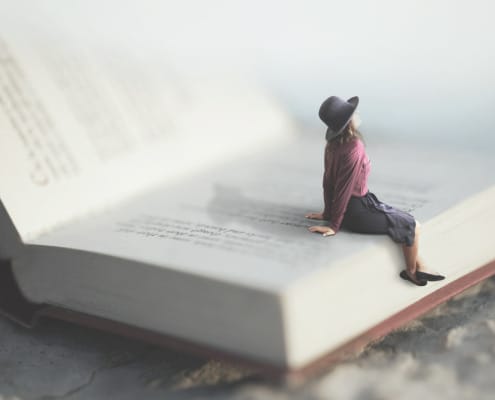 miniaturized woman sitting on the page of a book looking into the sky