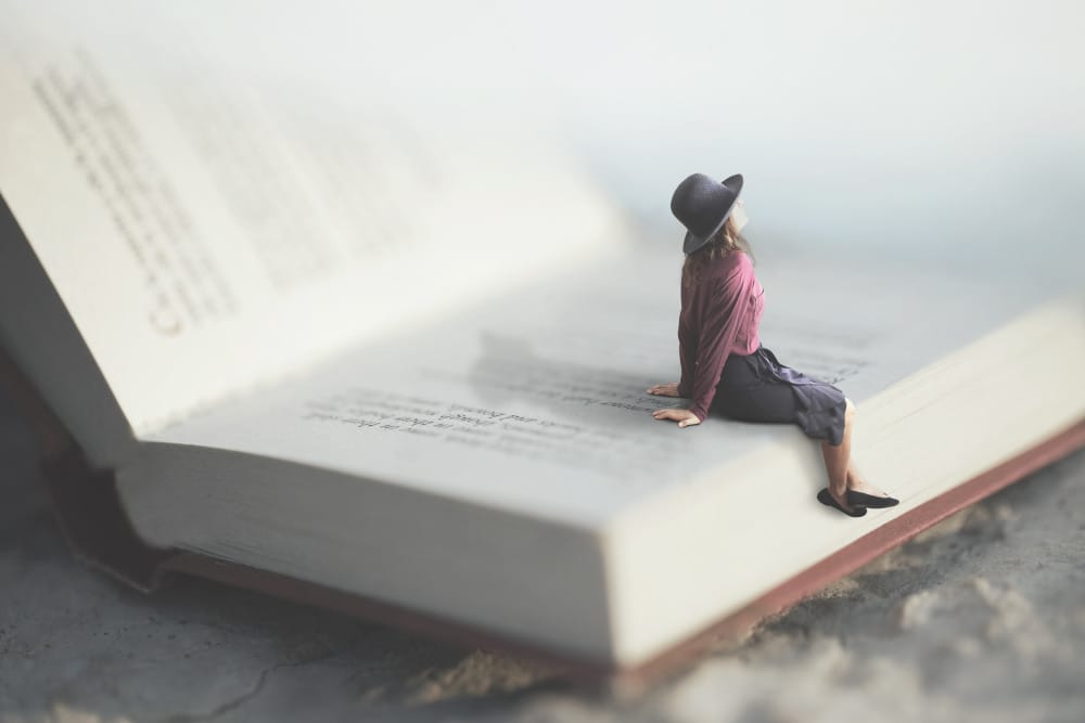 miniaturized woman sitting on the page of a book looking into the sky