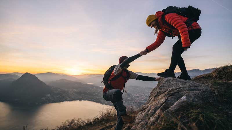 a female hiker helping offering a hand to a male hiker to help him climb up a rock